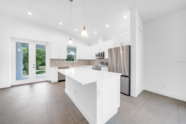 kitchen with appliances with stainless steel finishes, white cabinetry, hanging light fixtures, a center island, and vaulted ceiling