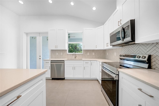 kitchen featuring vaulted ceiling, appliances with stainless steel finishes, light tile patterned flooring, white cabinetry, and sink