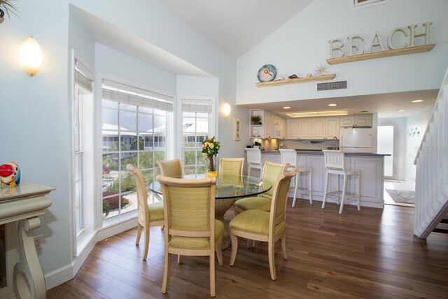 dining area with high vaulted ceiling and dark hardwood / wood-style floors