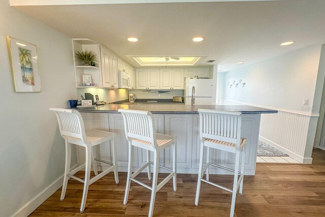 kitchen with white appliances, a breakfast bar area, light hardwood / wood-style floors, and kitchen peninsula