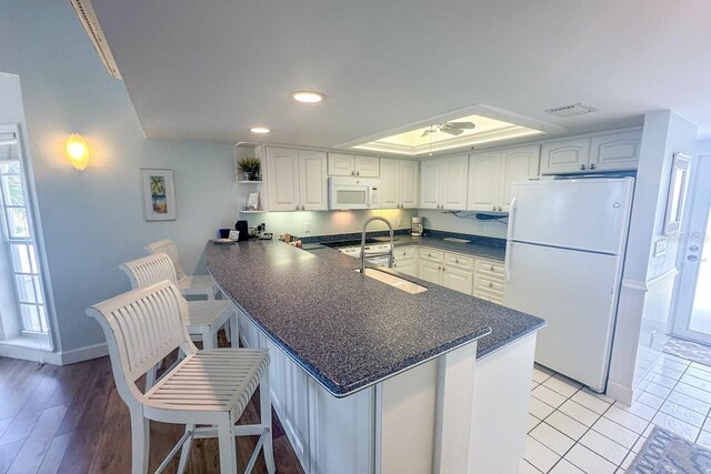 kitchen featuring kitchen peninsula, white appliances, light wood-type flooring, a breakfast bar area, and white cabinetry