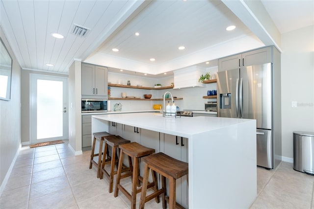 kitchen with appliances with stainless steel finishes, a kitchen bar, tasteful backsplash, gray cabinets, and a kitchen island with sink