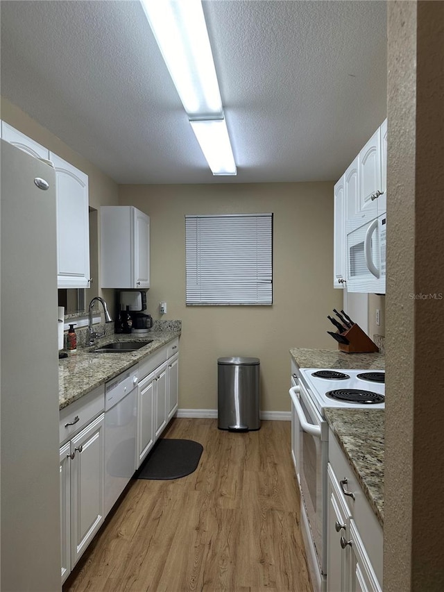 kitchen with white appliances, light stone countertops, white cabinetry, sink, and light hardwood / wood-style floors