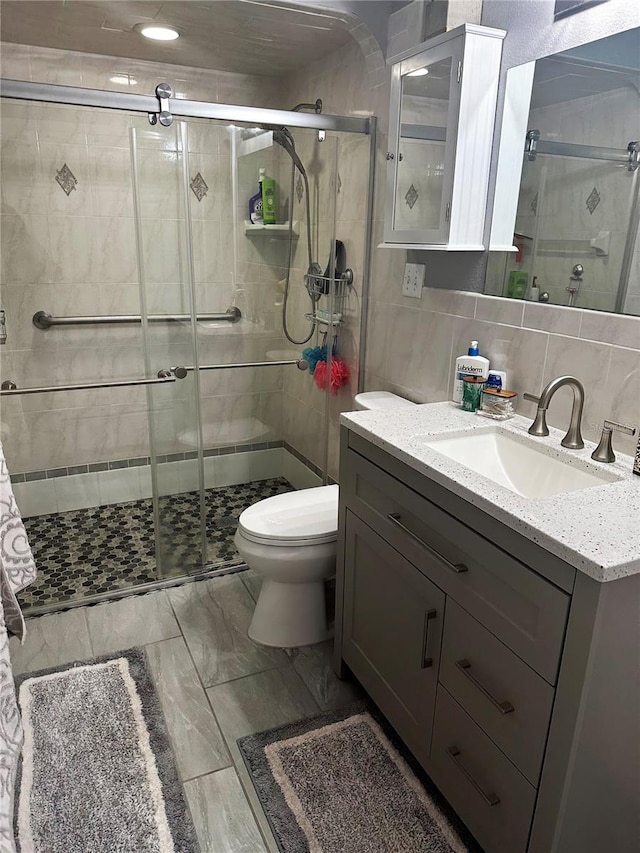 bathroom featuring a shower with door, tile walls, vanity, tasteful backsplash, and toilet