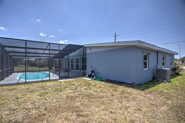 back of property featuring glass enclosure, a lawn, central air condition unit, and a patio area