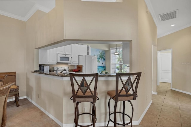 kitchen with white appliances, a kitchen breakfast bar, crown molding, kitchen peninsula, and white cabinetry