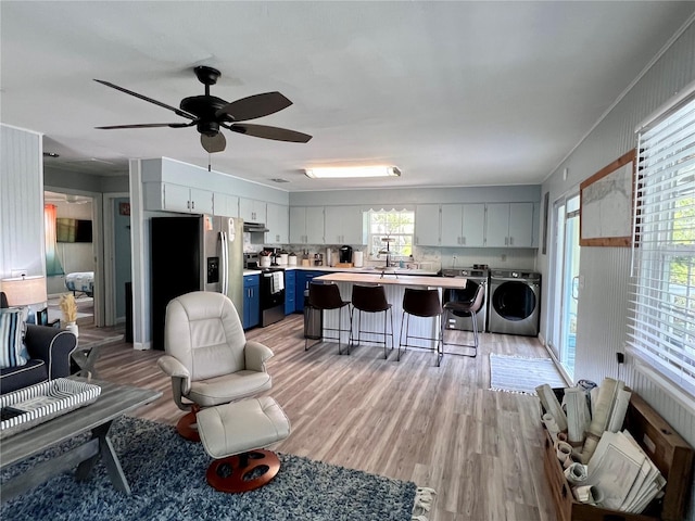 living room with a wealth of natural light, washer and clothes dryer, light wood-type flooring, and ceiling fan