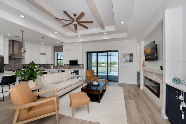 living room with ceiling fan, light hardwood / wood-style floors, a raised ceiling, and a high end fireplace