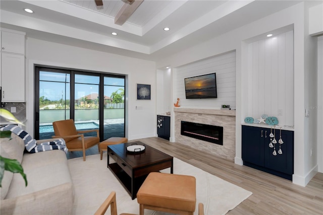 living room featuring beam ceiling, a stone fireplace, and light hardwood / wood-style flooring