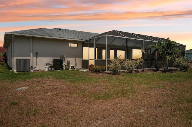 back house at dusk with central AC unit, a lanai, and a yard