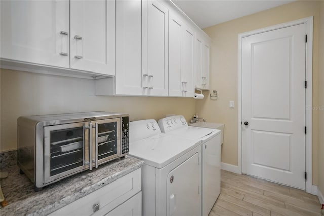 washroom featuring cabinets, washing machine and dryer, and light wood-type flooring