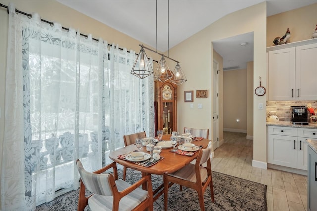 dining area featuring a chandelier, light wood-type flooring, and vaulted ceiling