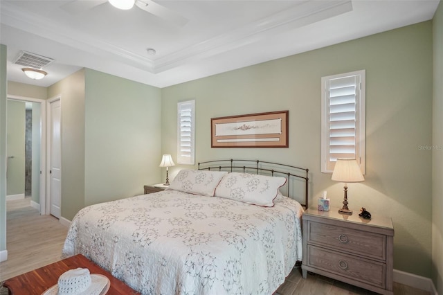 bedroom featuring a raised ceiling, ceiling fan, and light wood-type flooring