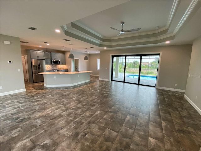 unfurnished living room featuring a tray ceiling, sink, ornamental molding, and ceiling fan