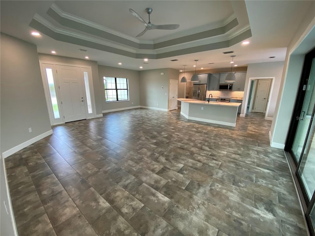 unfurnished living room with a tray ceiling, dark tile flooring, and crown molding