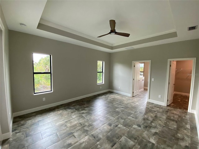 unfurnished bedroom with a walk in closet, a tray ceiling, and multiple windows