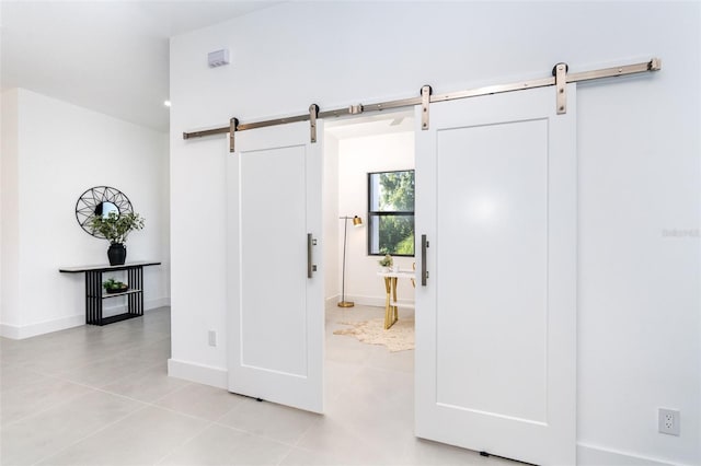 interior space with light tile patterned floors, a barn door, and baseboards