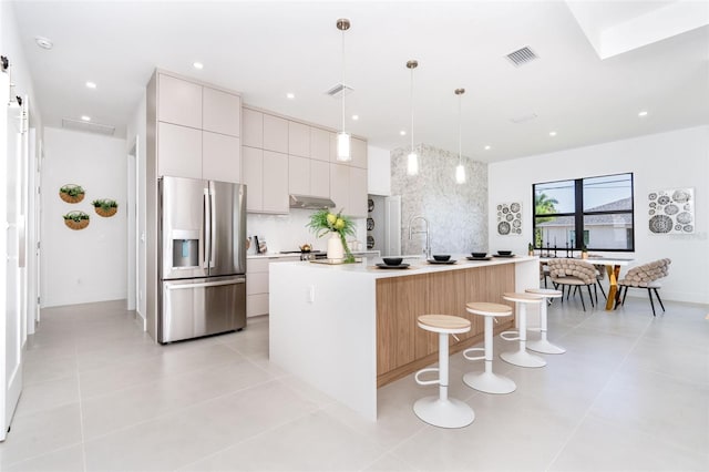 kitchen featuring white cabinets, light countertops, a center island with sink, stainless steel fridge with ice dispenser, and decorative light fixtures