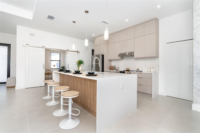 kitchen with a barn door, light countertops, modern cabinets, a center island with sink, and pendant lighting