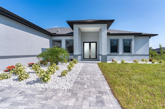 entrance to property with a yard, roof with shingles, and stucco siding