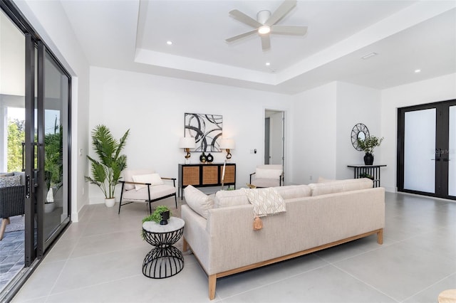 living room featuring light tile patterned floors, ceiling fan, a tray ceiling, french doors, and recessed lighting