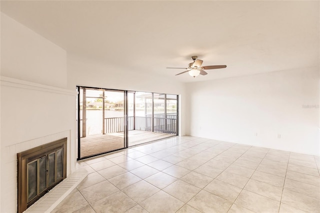 tiled empty room featuring a fireplace and ceiling fan