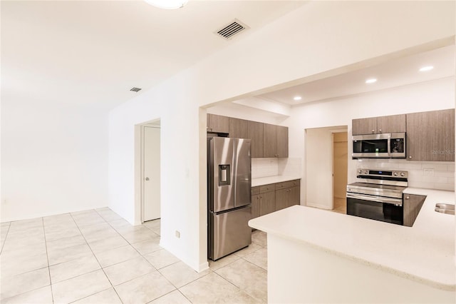 kitchen with decorative backsplash, appliances with stainless steel finishes, kitchen peninsula, and light tile patterned floors