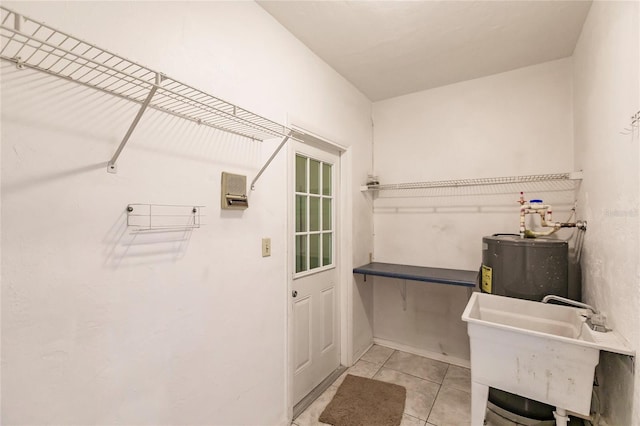 clothes washing area featuring light tile patterned flooring, sink, and water heater