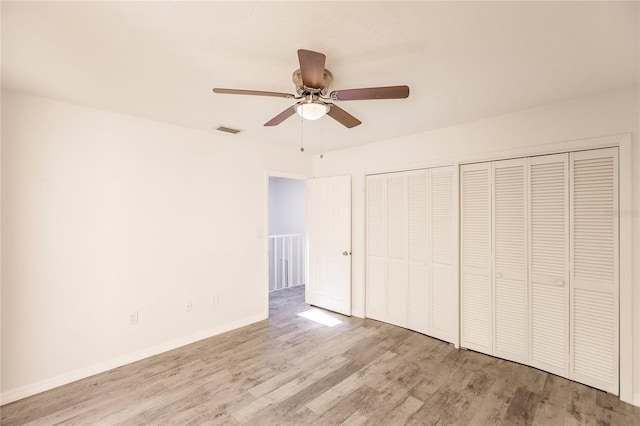 unfurnished bedroom featuring ceiling fan, light hardwood / wood-style floors, and multiple closets