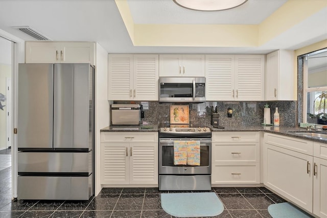 kitchen featuring dark stone counters, stainless steel appliances, backsplash, and dark tile floors