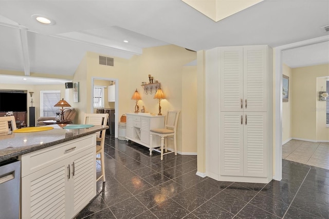 kitchen with white cabinetry, dark stone countertops, beam ceiling, dark tile flooring, and dishwasher