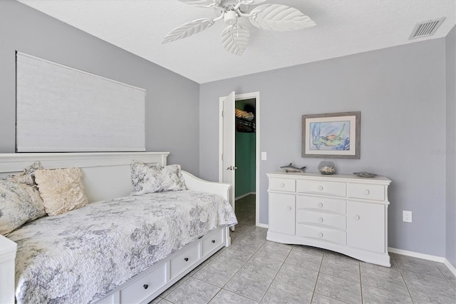 tiled bedroom with ceiling fan, a textured ceiling, and a spacious closet