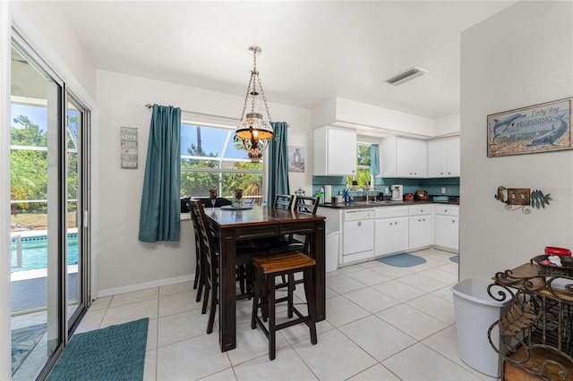 dining room featuring a healthy amount of sunlight, sink, a chandelier, and light tile floors