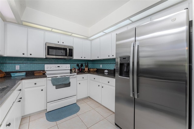 kitchen featuring dark stone counters, stainless steel appliances, backsplash, white cabinets, and light tile floors