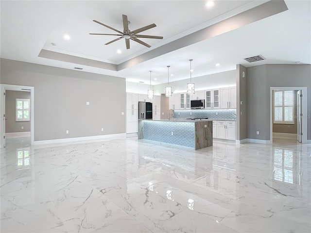 kitchen featuring white cabinetry, hanging light fixtures, a raised ceiling, an island with sink, and appliances with stainless steel finishes