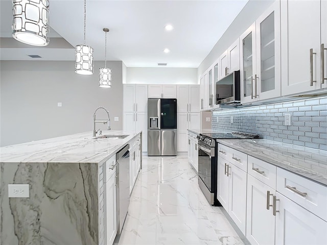 kitchen with light stone countertops, white cabinetry, sink, stainless steel appliances, and an island with sink