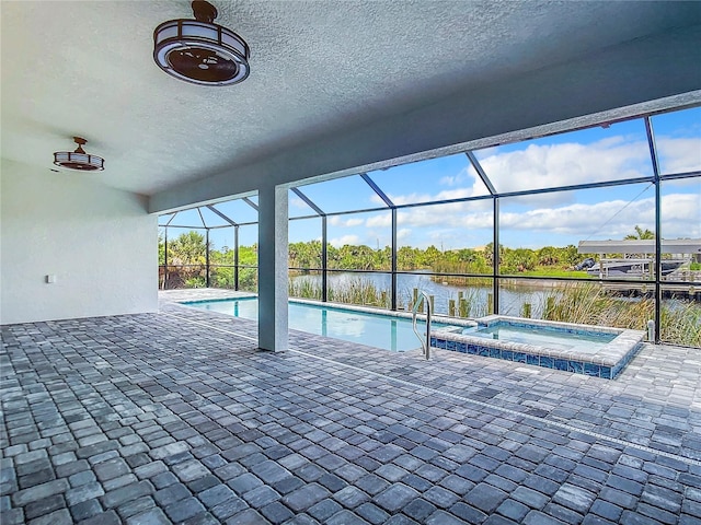 view of pool with an in ground hot tub, a water view, glass enclosure, and a patio area