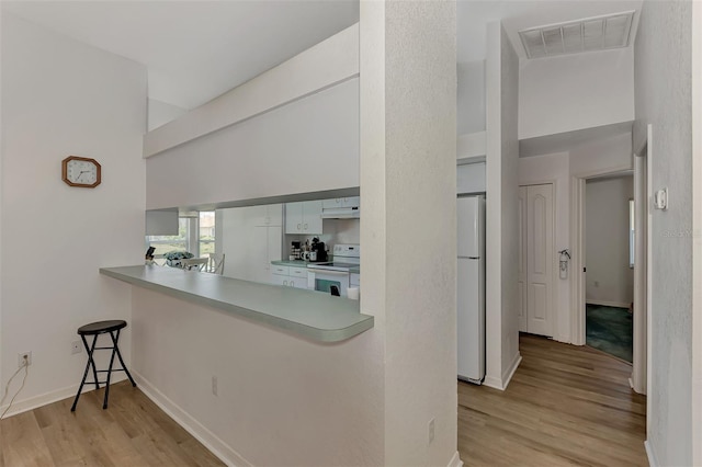 kitchen with white appliances, white cabinetry, and light hardwood / wood-style flooring