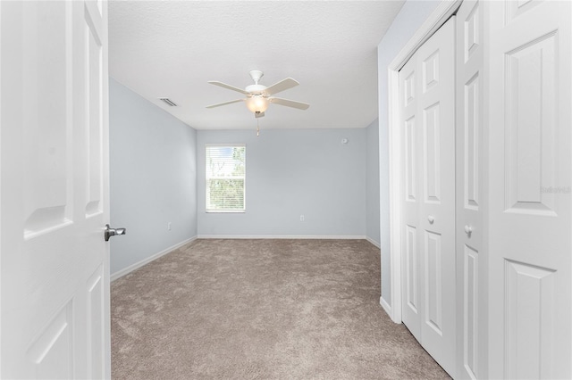 unfurnished bedroom featuring light carpet, ceiling fan, a closet, and a textured ceiling