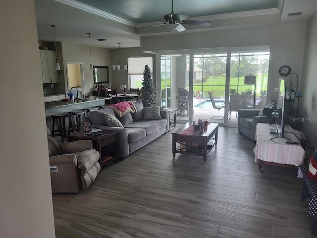 living room with dark wood-type flooring, a raised ceiling, and ceiling fan