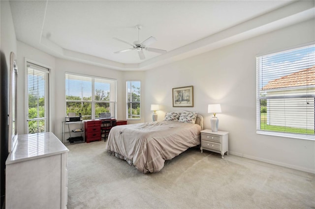 carpeted bedroom with a raised ceiling, multiple windows, and ceiling fan