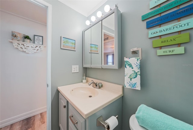 half bathroom with baseboards, vanity, toilet, and wood finished floors