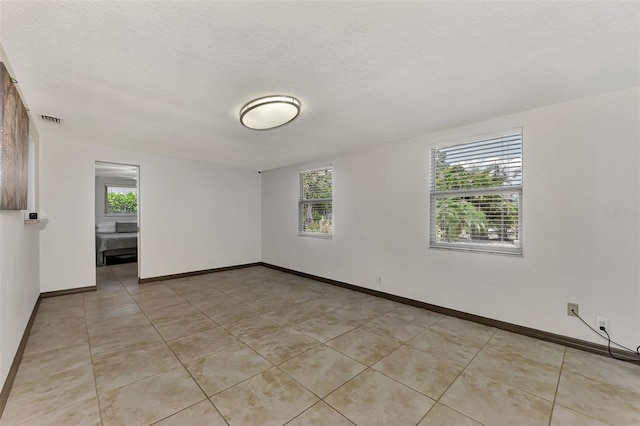 tiled empty room featuring a textured ceiling and plenty of natural light