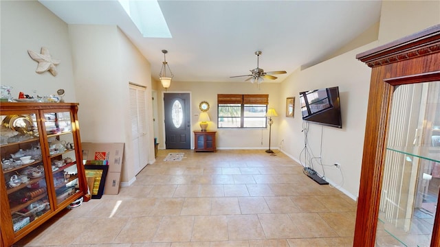 foyer entrance with light tile patterned flooring, ceiling fan, and vaulted ceiling with skylight