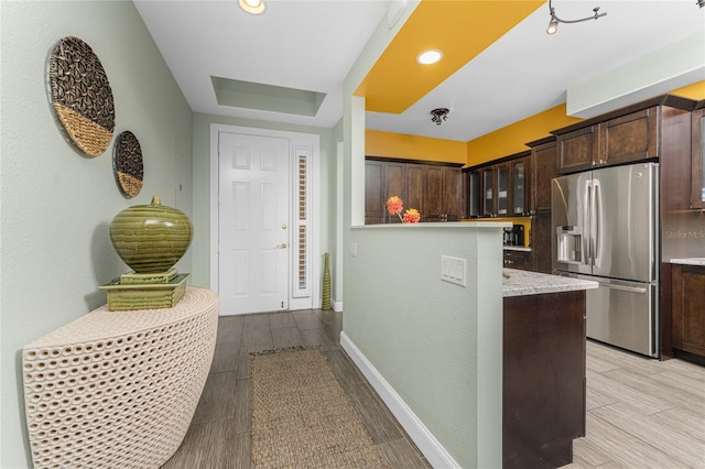 kitchen featuring light wood-type flooring, stainless steel refrigerator with ice dispenser, dark brown cabinetry, and light stone counters