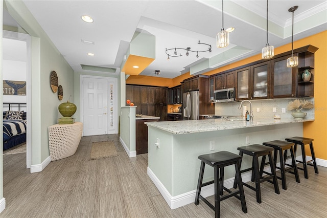 kitchen featuring backsplash, hanging light fixtures, dark brown cabinets, kitchen peninsula, and stainless steel appliances