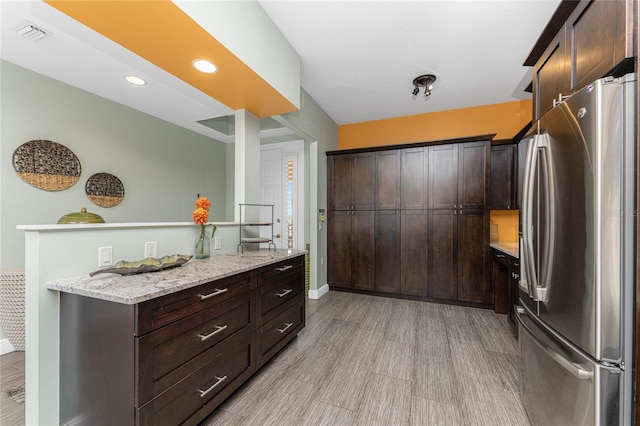 kitchen featuring dark brown cabinets, light stone counters, stainless steel refrigerator, and light hardwood / wood-style flooring