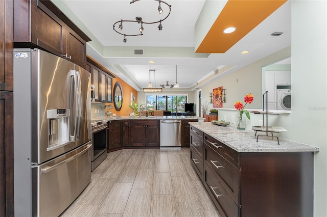 kitchen featuring light stone countertops, decorative light fixtures, washer / dryer, kitchen peninsula, and stainless steel appliances