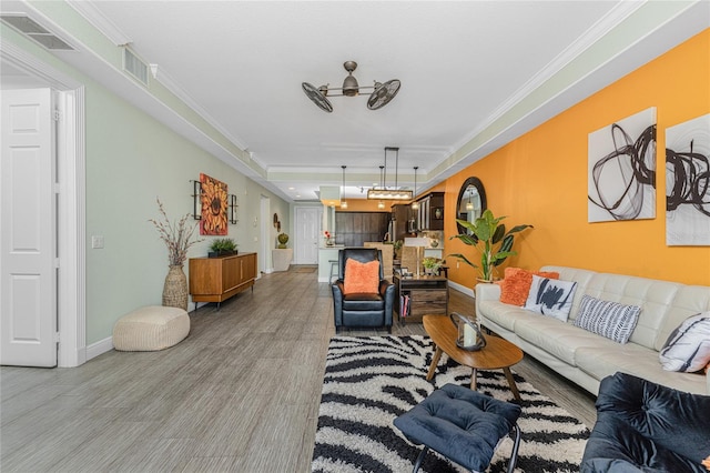 living room featuring hardwood / wood-style flooring, ceiling fan, ornamental molding, and a tray ceiling