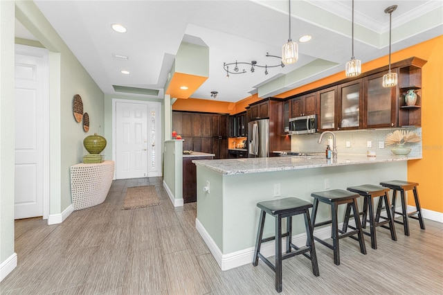 kitchen with a breakfast bar, tasteful backsplash, dark brown cabinets, kitchen peninsula, and stainless steel appliances